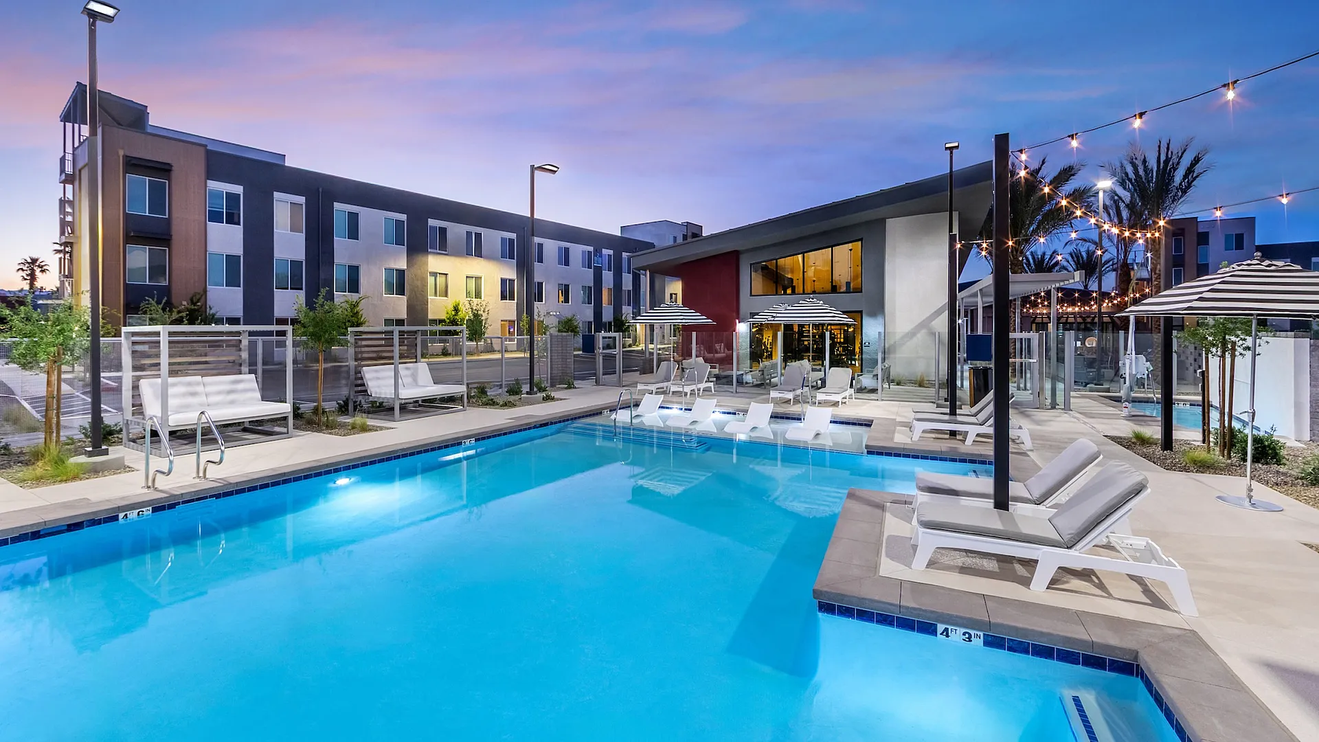 Modern apartment complex featuring a stunning outdoor pool area with stylish lounge chairs and elegant lighting at dusk.