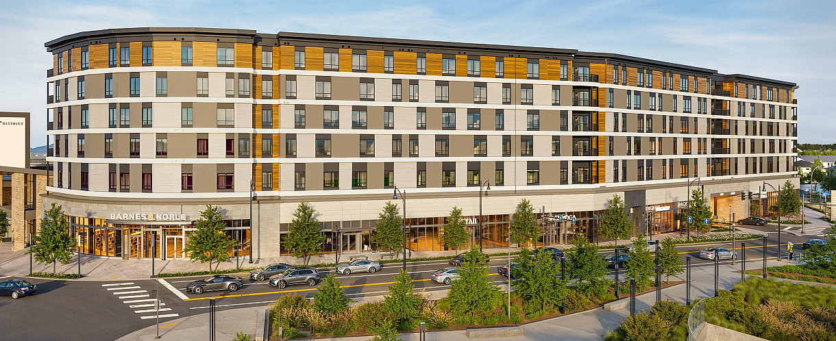 Modern multi-story residential and retail complex with vibrant ground-level shops, surrounded by lush greenery and bustling streets.