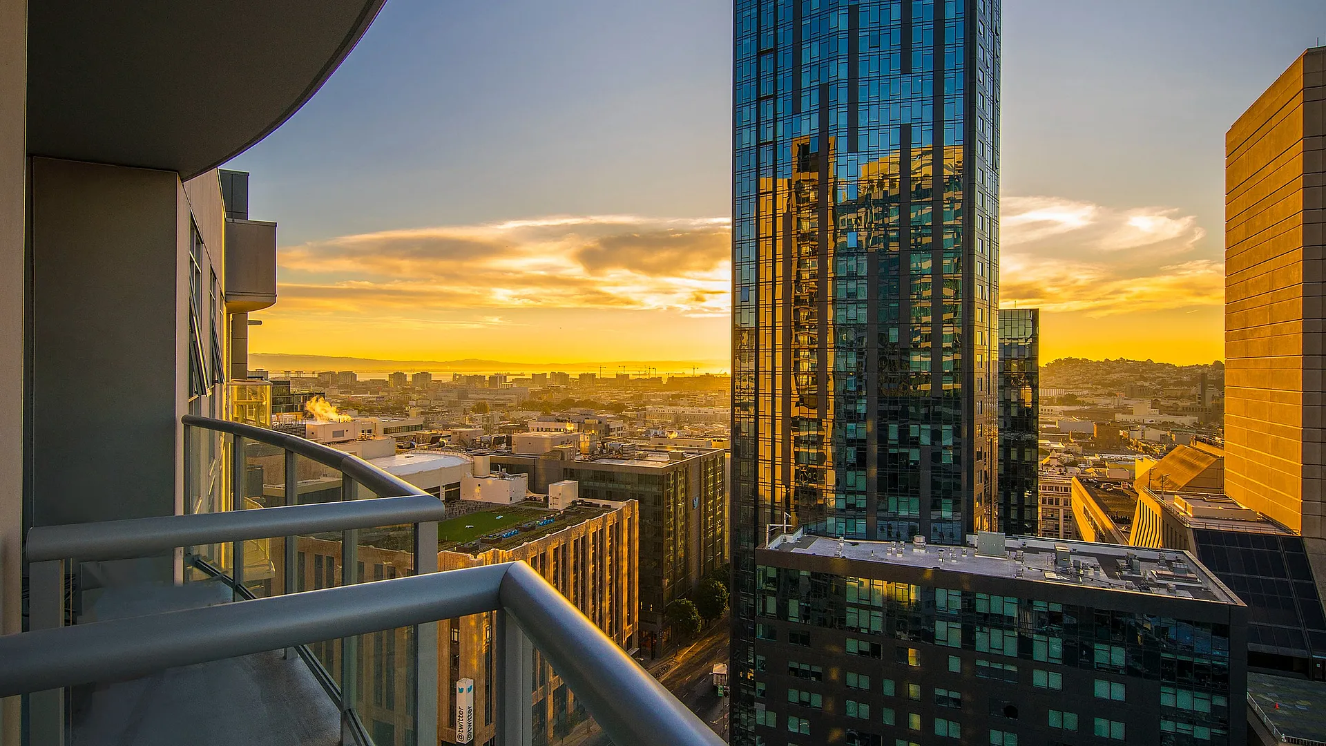 Breathtaking cityscape view from a modern apartment balcony, showcasing a vibrant sunset and a towering glass building.