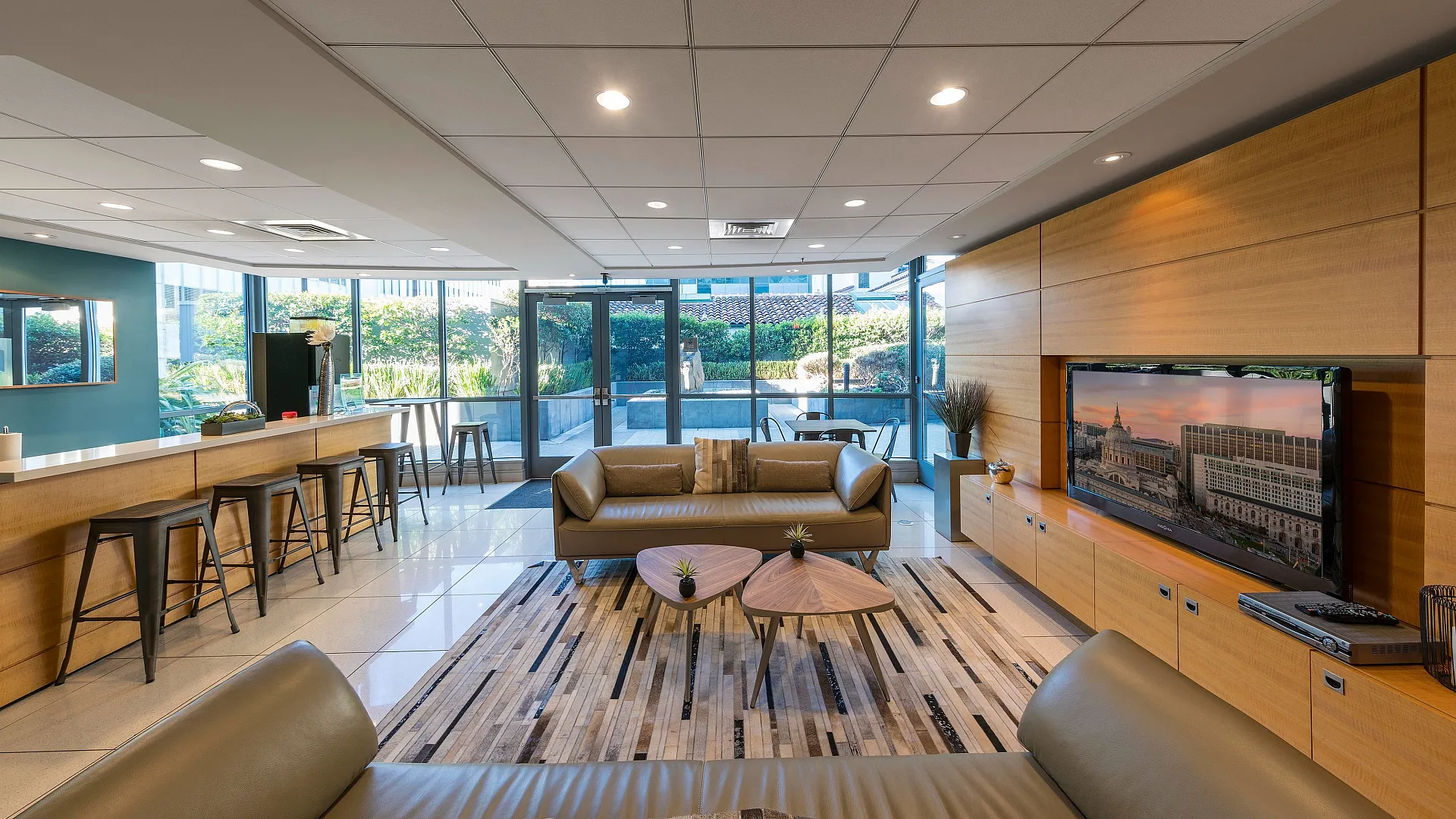 Modern living area with stylish seating, sleek wooden TV unit, and large windows offering a lush garden view.