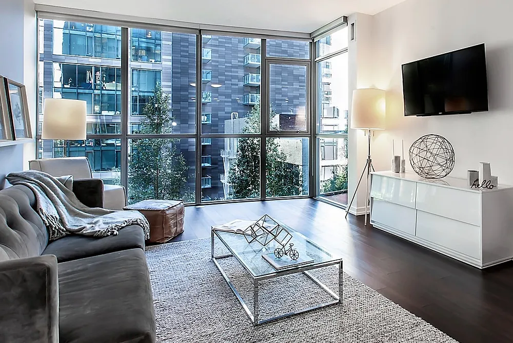 Modern apartment living room with floor-to-ceiling windows, elegant gray sofa, and chic decor, offering stunning city views.