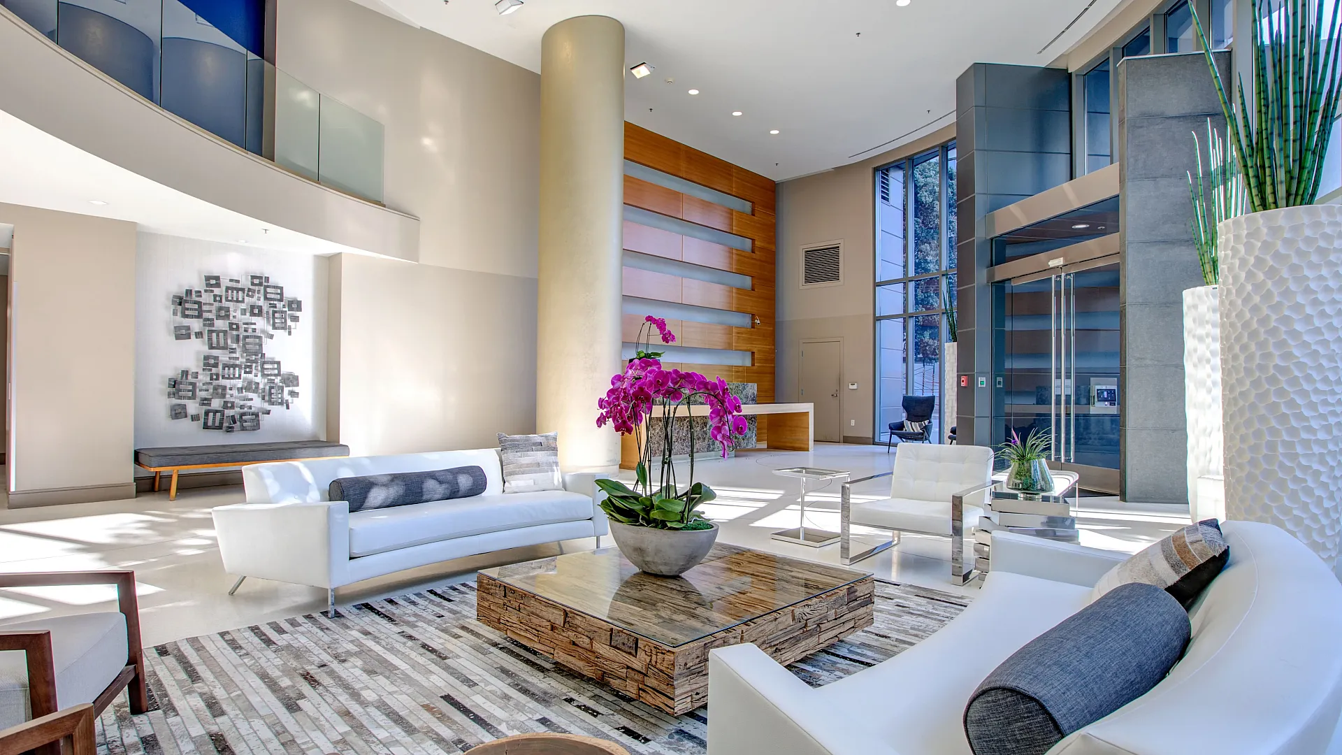 Luxurious modern apartment lobby featuring elegant seating, large windows, and vibrant decor with fresh orchids.