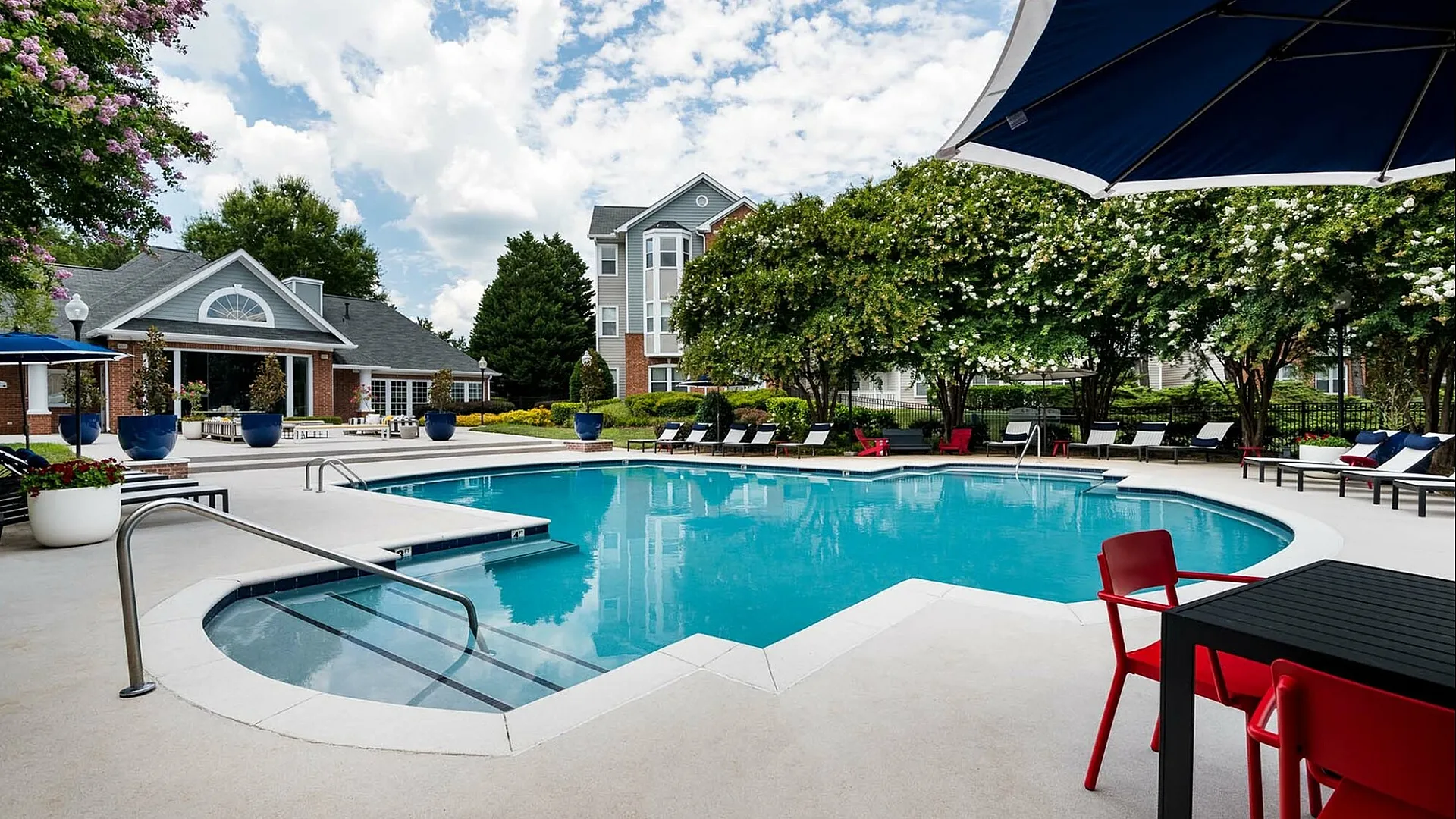 Lush summer oasis featuring a pristine swimming pool surrounded by stylish loungers and vibrant red seating, ideal for relaxation and outdoor entertaining.