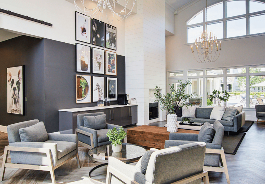 Elegant living room featuring sophisticated decor, modern gray sofas, ample natural light, lush plants, and stylish artwork on dark accent walls, all beneath a stunning chandelier.