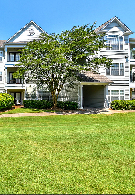 Charming three-story apartment building with fresh white siding, lush green landscaping, and abundant natural light, offering a serene and inviting living space.