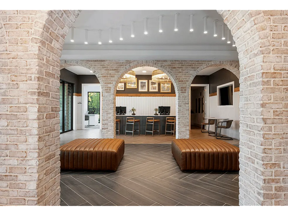 Stunning apartment lounge featuring elegant brick arches, sleek leather seating, and a modern communal workspace.
