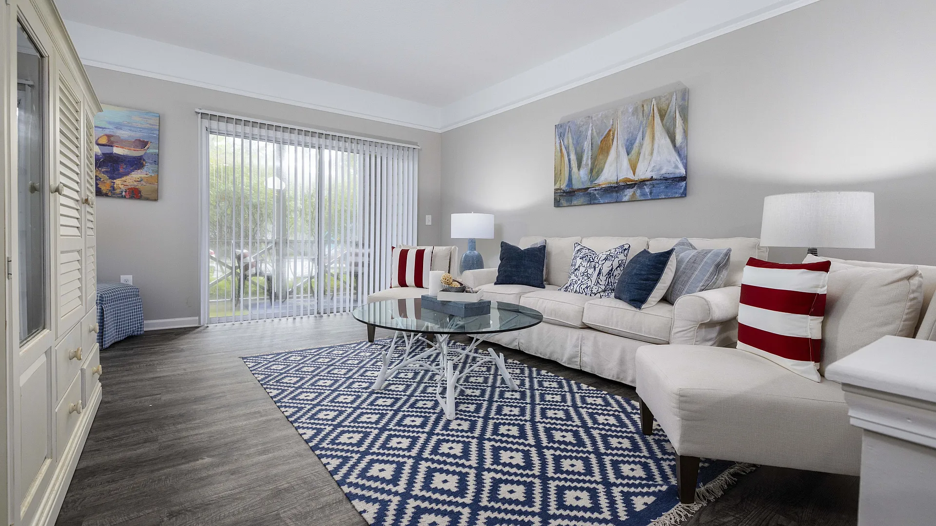 Inviting living room with modern decor, featuring a cozy beige sofa, vibrant blue and red cushions, and an elegant glass coffee table atop a stylish geometric rug.