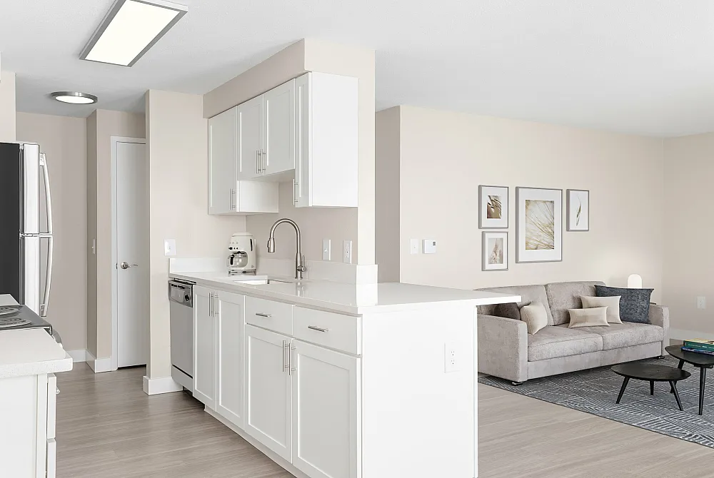 Inviting open-concept kitchen and living room with modern white cabinetry, sleek countertops, and cozy seating area adorned with stylish artwork.
