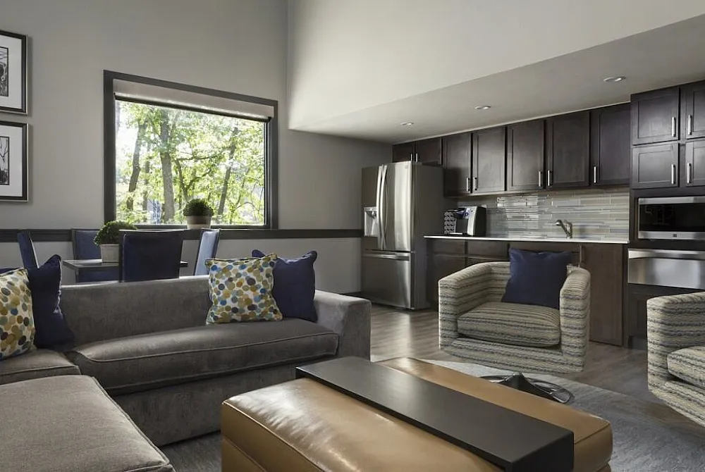 Contemporary open-plan living room with modern kitchen, inviting sofa, stylish armchairs, and large window with scenic view.