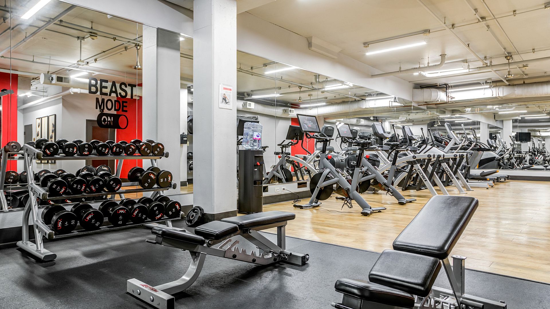 Modern gym with state-of-the-art fitness equipment, including treadmills, dumbbells, and benches, featuring large mirrors and vibrant red accents.