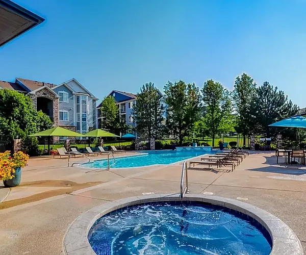 Lush apartment complex featuring a sparkling swimming pool, relaxing hot tub, and vibrant outdoor seating under clear blue skies.