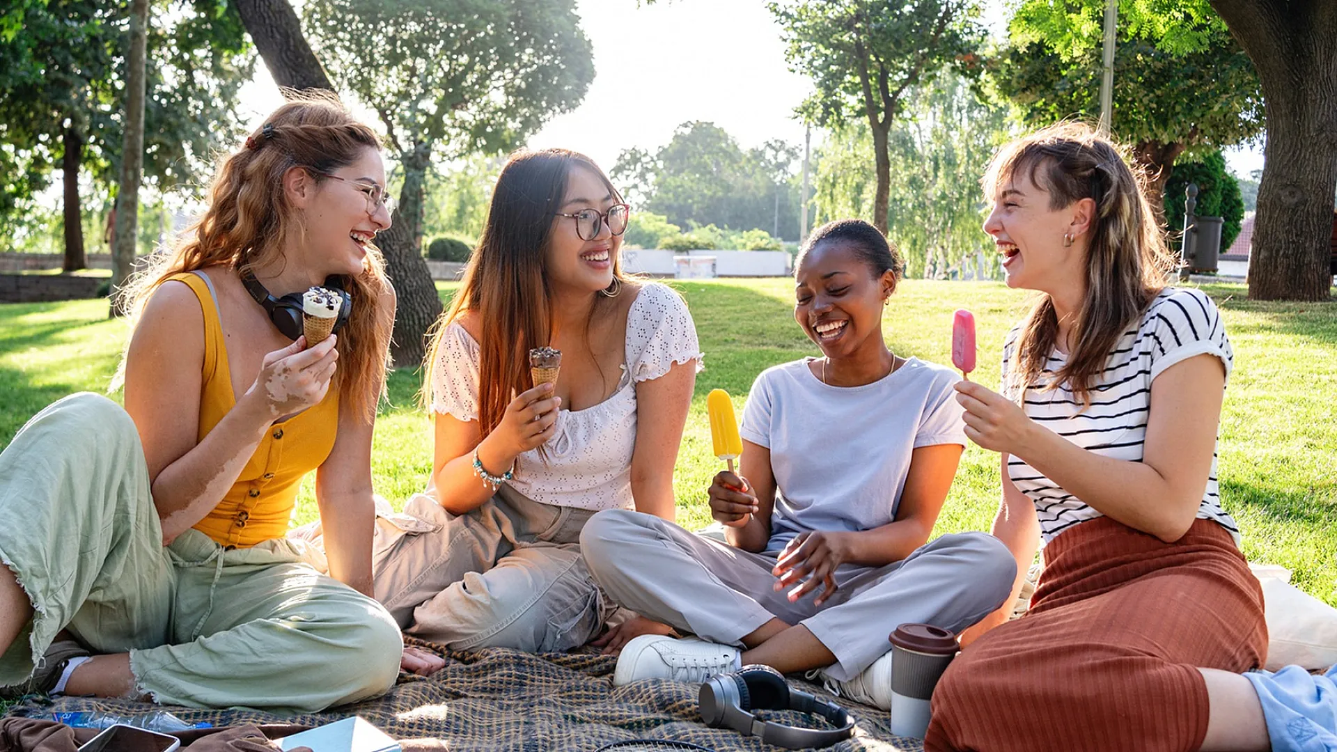 Joyful group of friends enjoying ice cream on a sunny day in a green park, surrounded by laughter and nature.