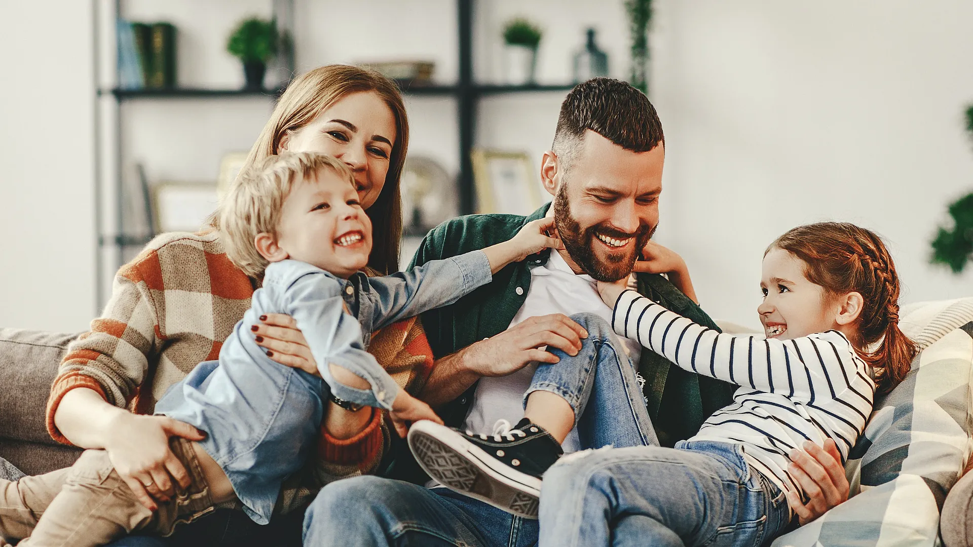 Joyful family of four relaxing on a cozy sofa in a warmly decorated living room, exuding happiness and togetherness.
