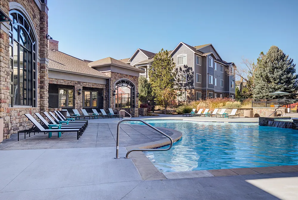 Luxurious apartment complex with a sparkling outdoor pool, elegant stone accents, and stylish lounge chairs, offering a serene and upscale living experience.