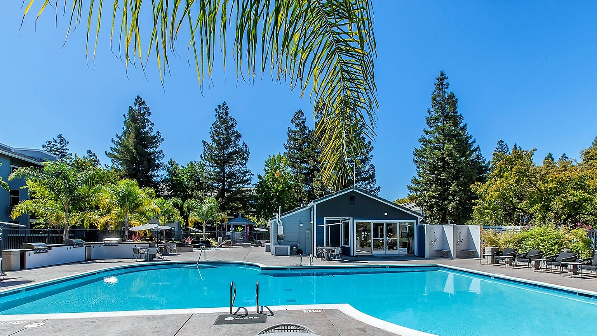Luxurious poolside retreat featuring sparkling blue waters, elegant patio seating, and lush green landscaping.