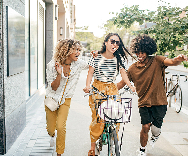Three friends enjoying a joyful day outdoors, laughing and biking down a sunlit street.