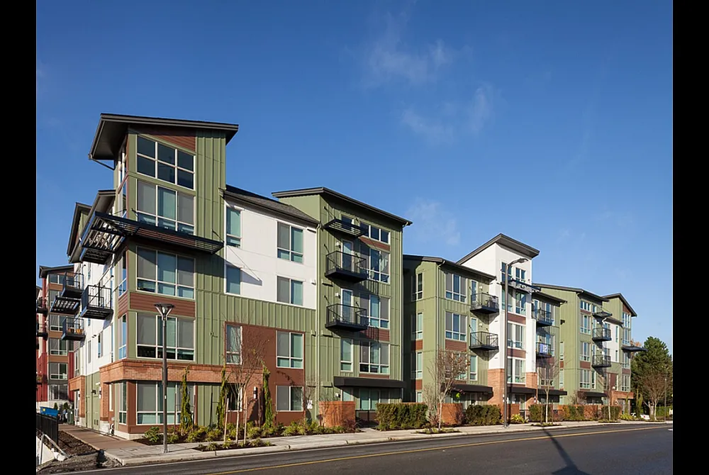 Modern multi-story apartment building with stylish balconies and contemporary design set against a clear blue sky.