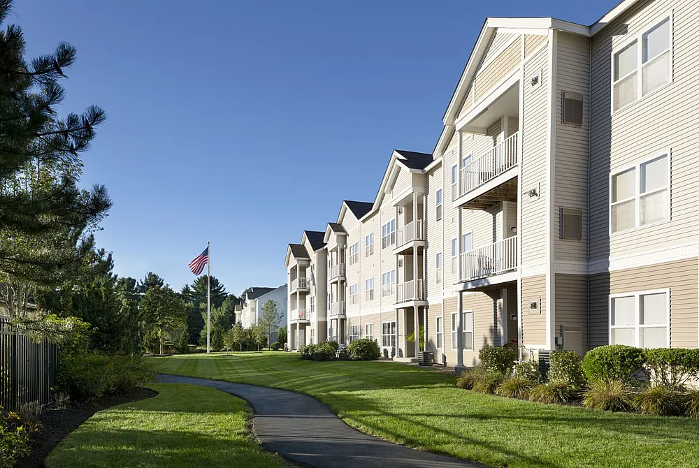 Modern apartment complex with charming balconies, lush landscaped grounds, and an inviting path under a clear blue sky.