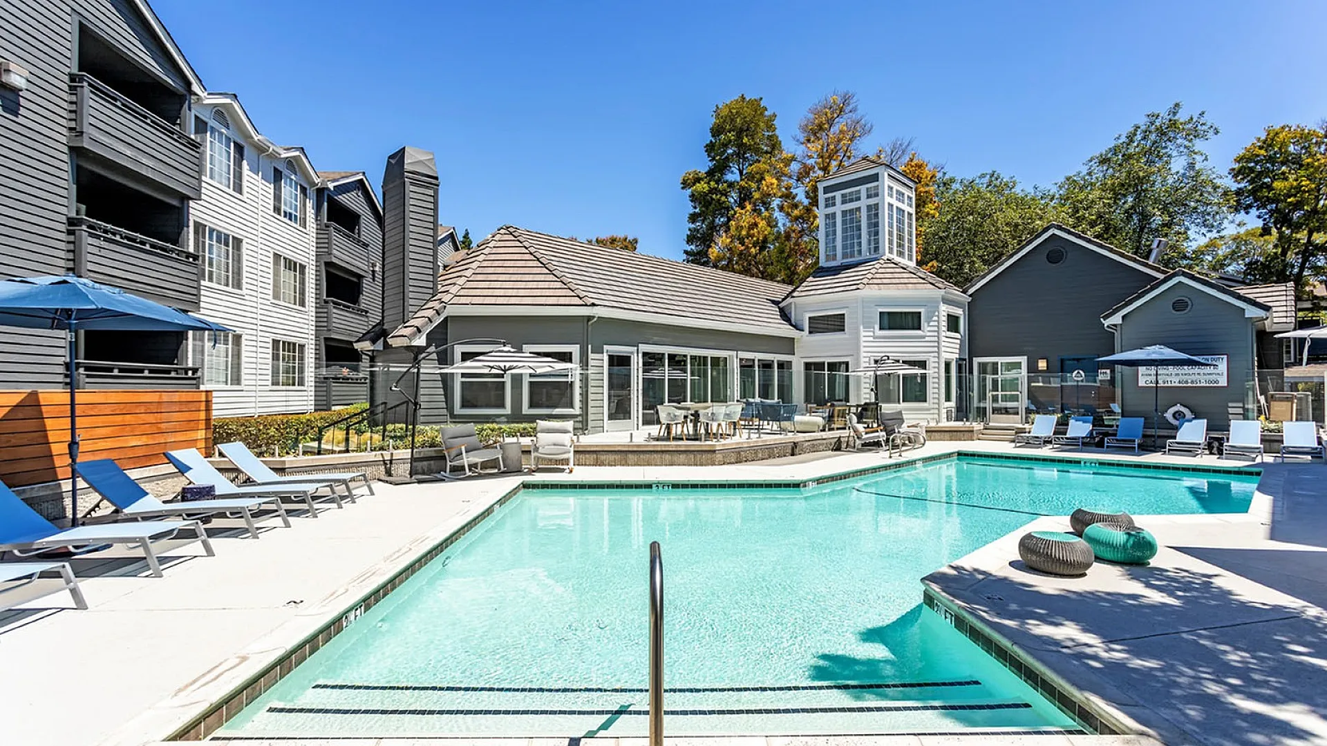 Luxurious apartment complex showcasing a sparkling swimming pool, ample lounge chairs, and modern architecture surrounded by lush greenery.