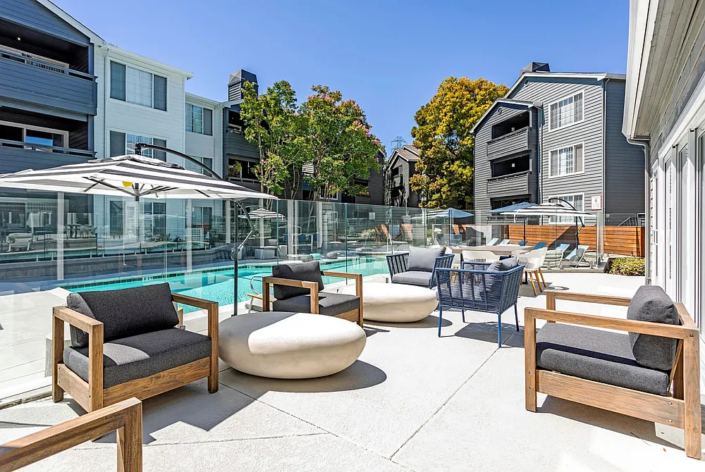 Luxurious outdoor pool area with modern seating and vibrant greenery, ideal for relaxation and entertainment in a stylish apartment complex.