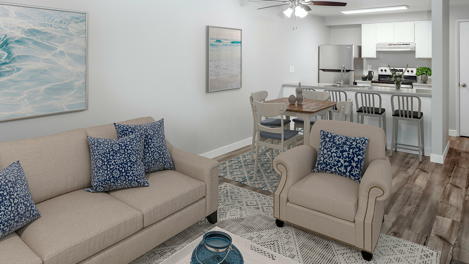 Inviting open-concept living space featuring a cozy beige sofa with blue patterned cushions, a modern kitchen with stainless steel appliances, and a stylish dining area under a ceiling fan.