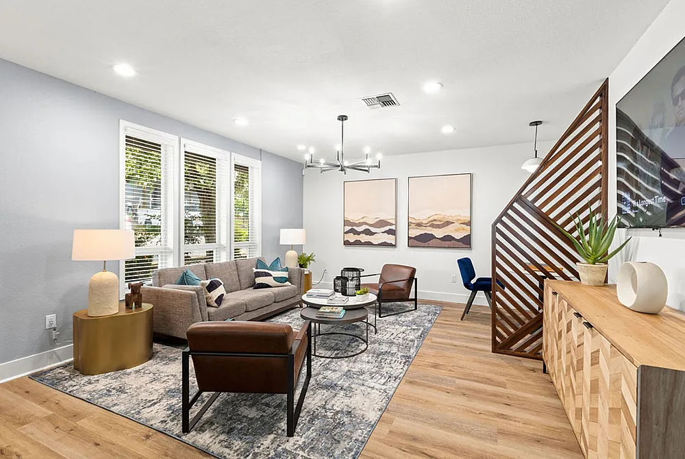 Elegant living room with modern decor, featuring a cozy gray sofa, stylish brown chairs, and chic wall art, complemented by a warm wooden floor and abundant natural light.
