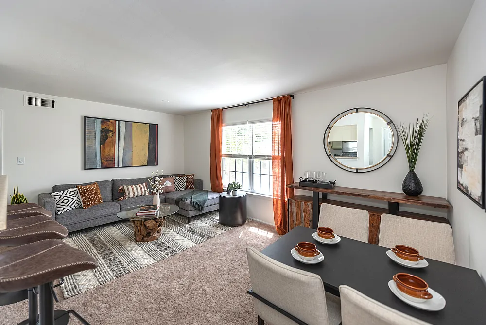 Inviting and stylish living room with modern decor, featuring a cozy sectional sofa, vibrant wall art, and a sleek dining area with elegant settings, bathed in natural light from large windows.