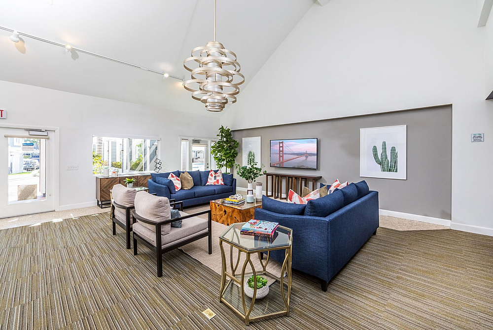Modern living room with elegant chandelier, vibrant blue sofas, stylish decor, and abundant natural light.