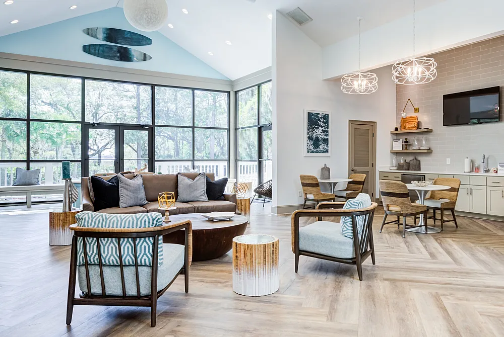 Bright and modern community room with stylish seating, elegant lighting, and large windows overlooking lush greenery.