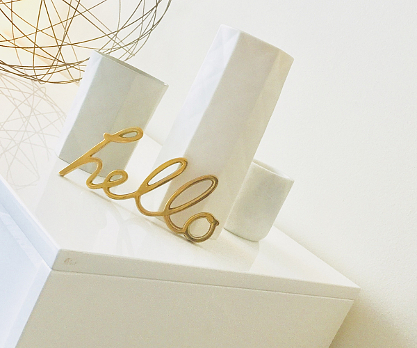Chic modern decor featuring a white vase set and gold wire orb, complemented by a stylish 'hello' sign on a sleek white surface.