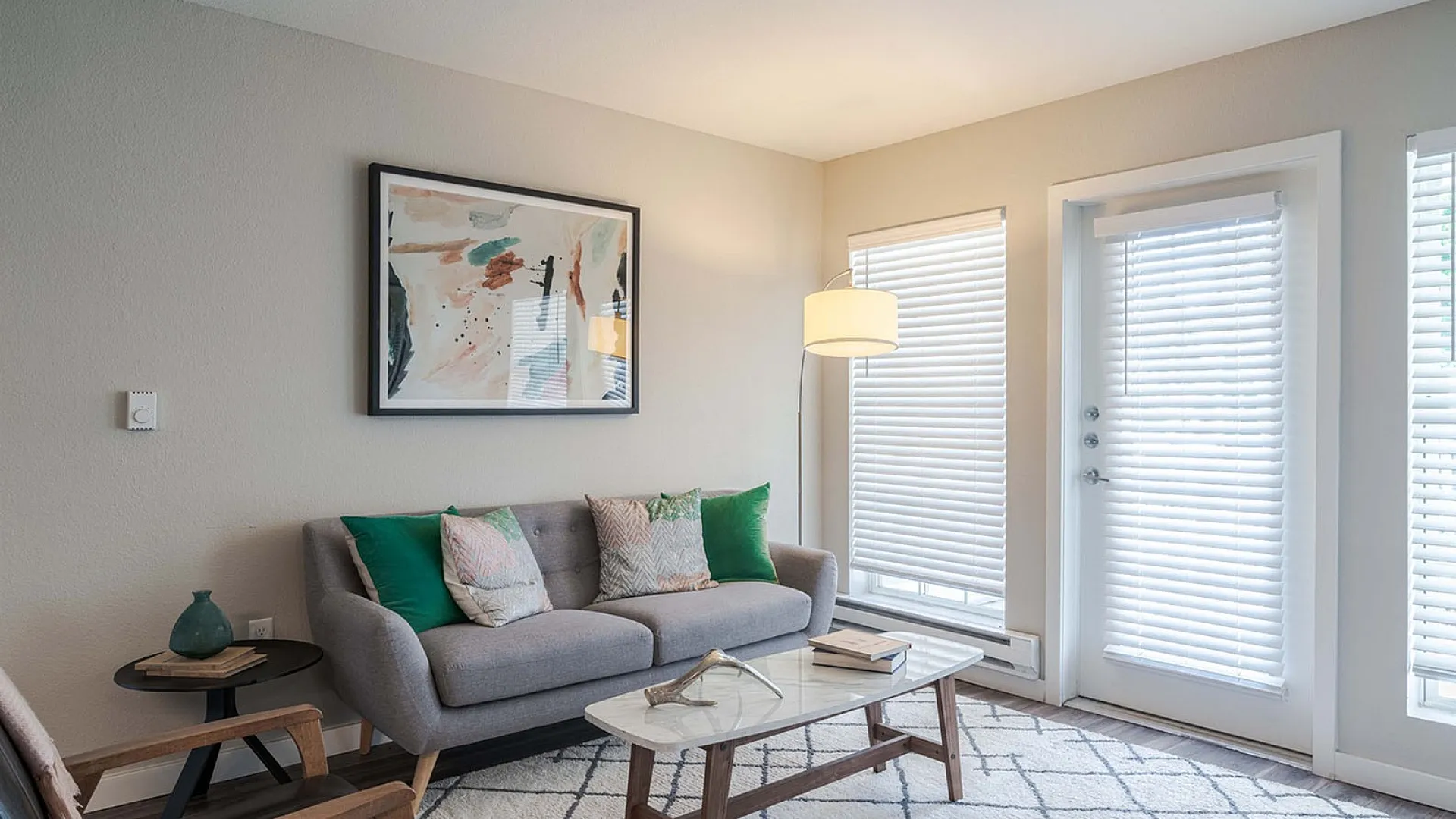 Inviting living room with modern decor, cozy gray sofa, colorful cushions, stylish artwork, and abundant natural light through large windows.