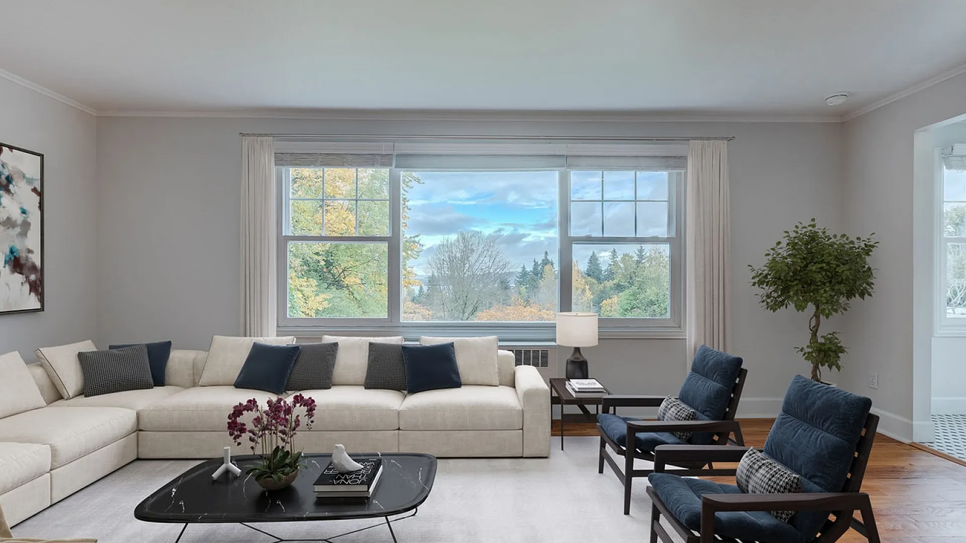 Bright and airy living room with a large window showcasing scenic outdoor views, modern beige sectional, stylish armchairs, and elegant decor.