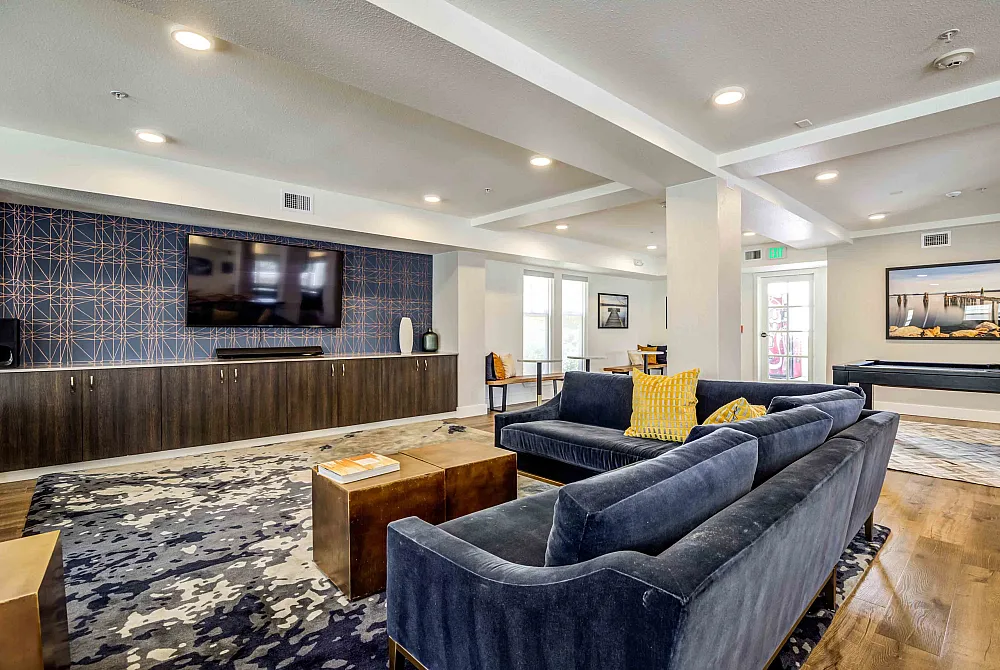 Modern and inviting living room with stylish navy sofas, bright yellow accent pillows, and a sleek entertainment center with a large TV, perfect for relaxation and social gatherings.