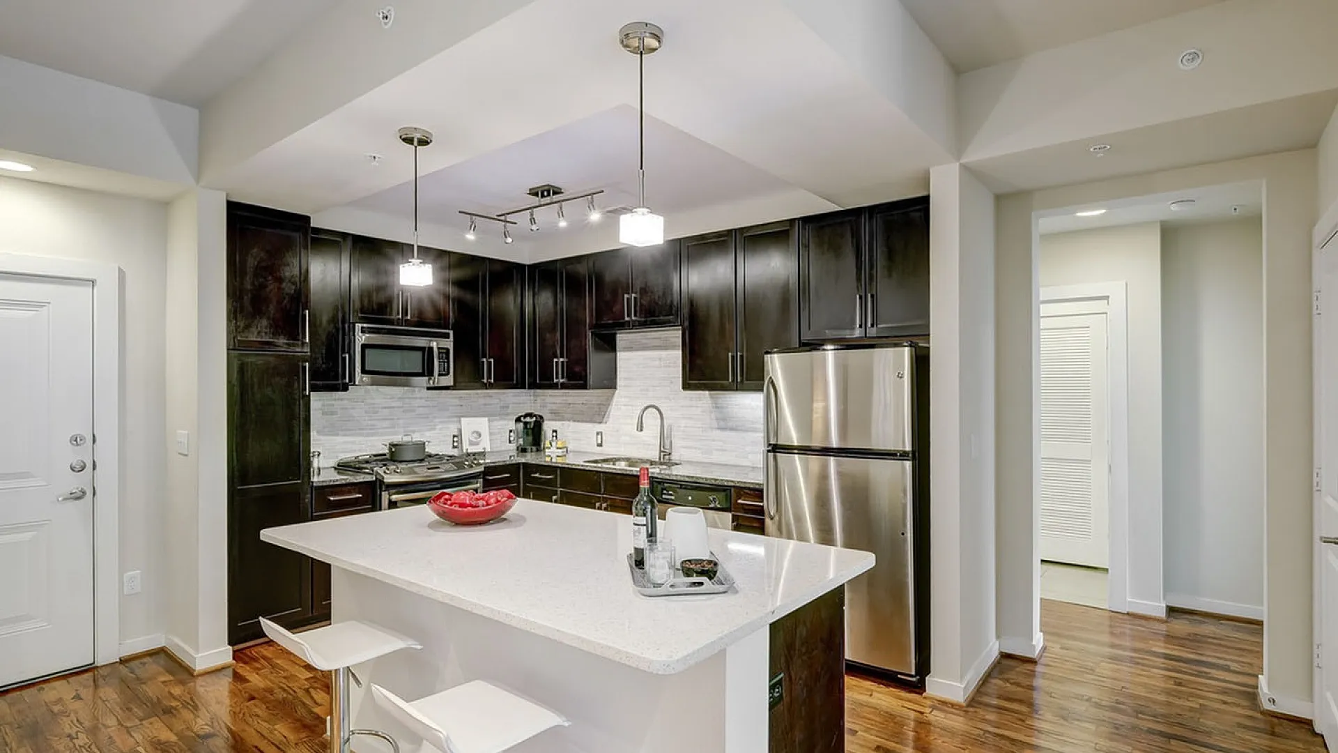 Modern kitchen with sleek dark cabinets, stainless steel appliances, and a spacious white island with contemporary bar stools on polished wooden floors.