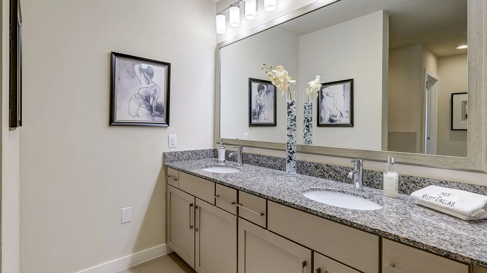 Elegant bathroom featuring a dual-sink granite countertop, chic wall art, and contemporary lighting fixtures, offering a luxurious spa-like experience.