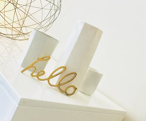 Chic modern decor featuring a geometric wire lamp and elegant 'hello' sign on a sleek white surface.