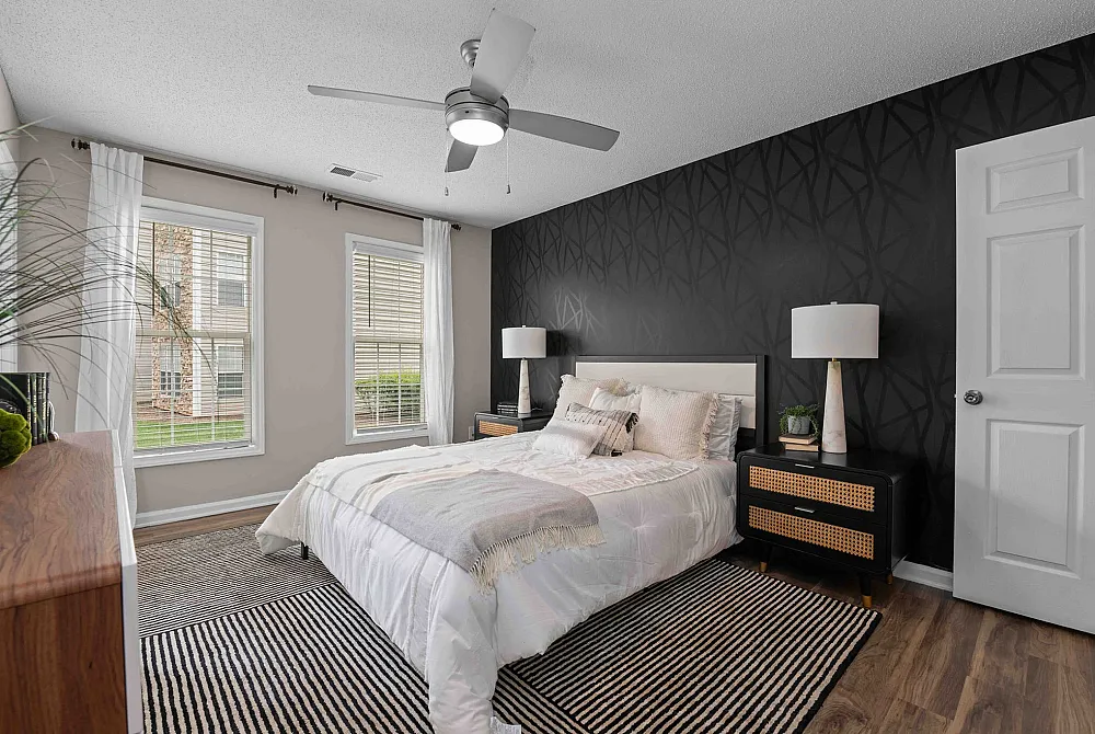 Elegant bedroom with modern black accent wall, plush bedding, and natural light streaming through large windows.