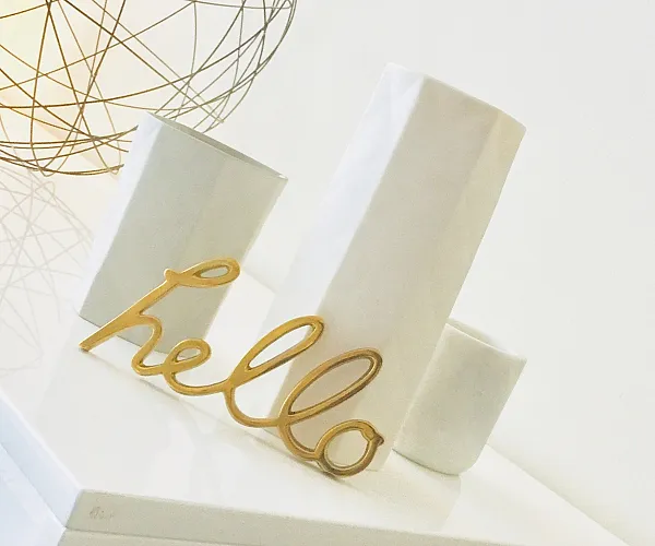 Elegant decorative setup featuring a stylish wire lamp, sleek modern vases, and a welcoming 'hello' sign in a chic apartment interior.