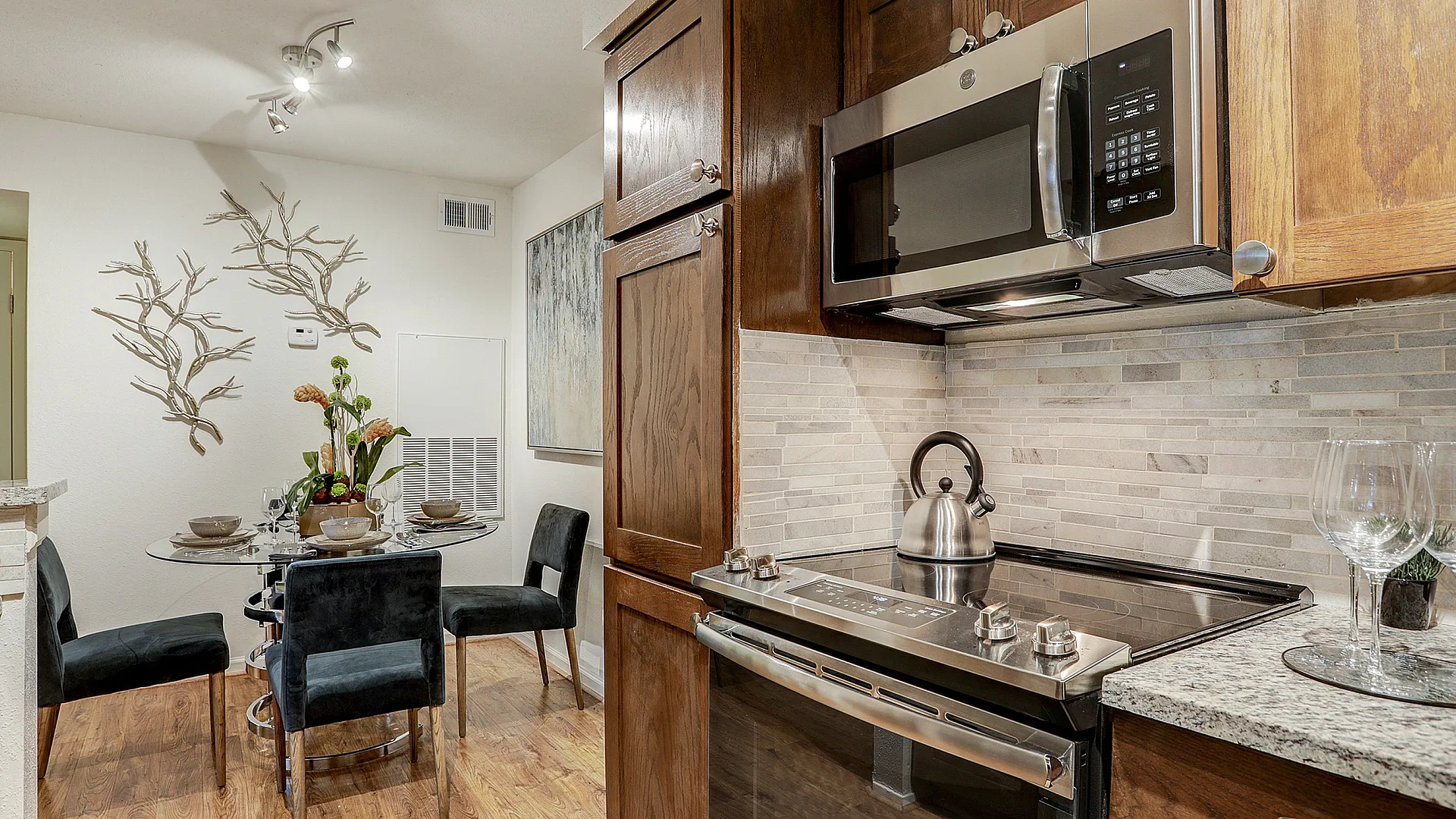 Cozy kitchen with modern appliances, elegant wooden cabinetry, and a chic dining area showcasing a glass table and plush chairs.