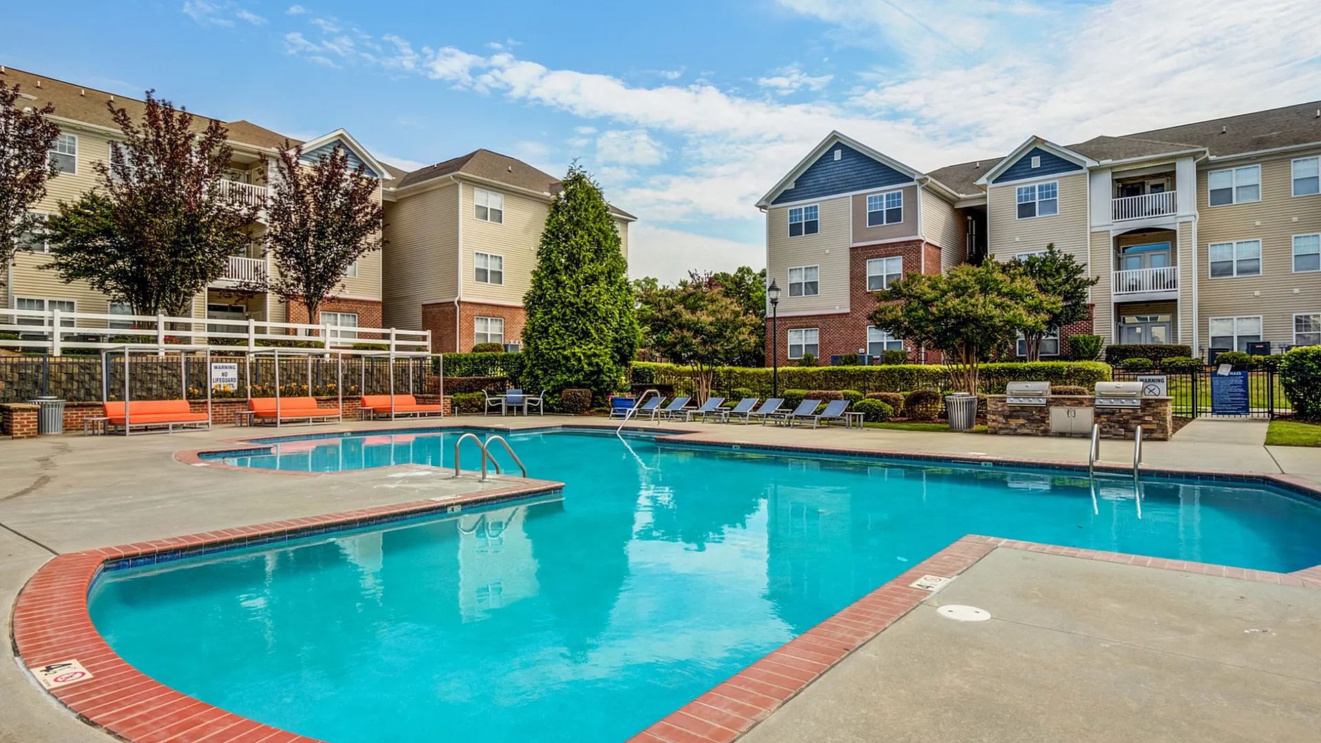 Inviting apartment complex with a sparkling pool, surrounded by modern buildings and lush landscaping.