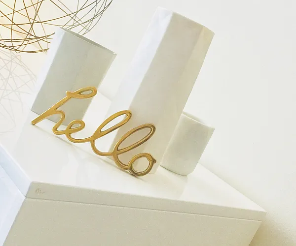 Chic minimalist decor with geometric pendant lamp, modern vases, and a stylish 'hello' sign on a sleek white surface.