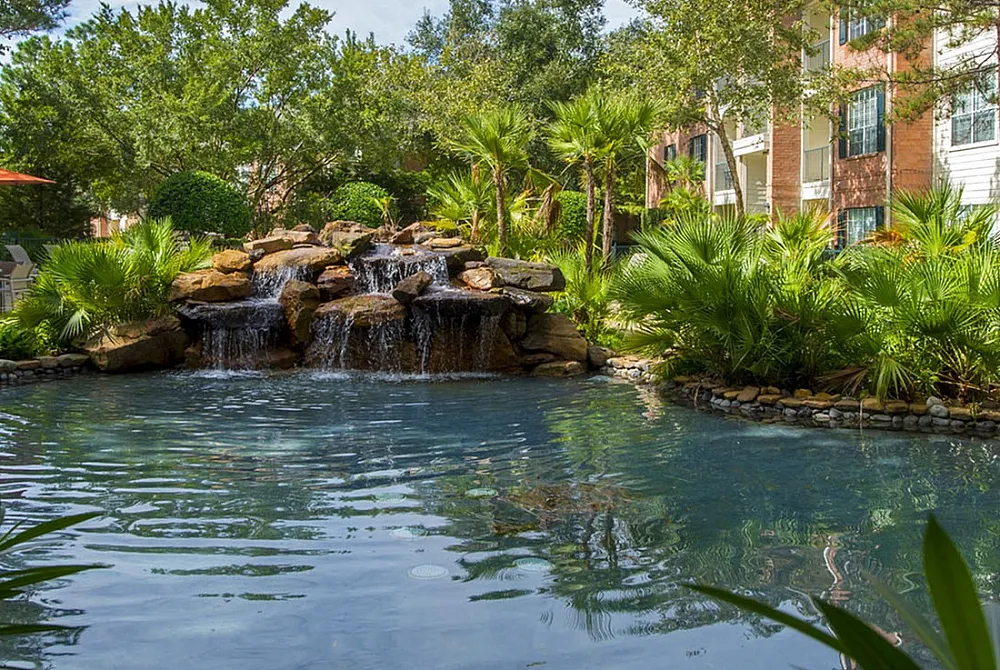 Serene apartment complex with lush greenery and a picturesque cascading waterfall into a tranquil pond.