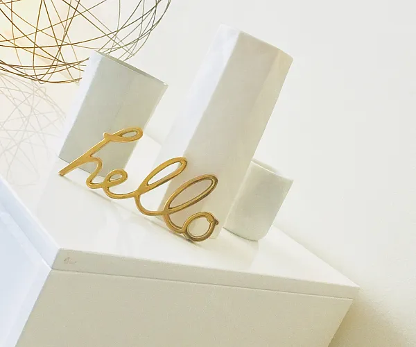 Chic and modern decor featuring a sleek white surface with elegant vases and a stylish 'hello' sculpture, accented by a warm, geometric lamp.
