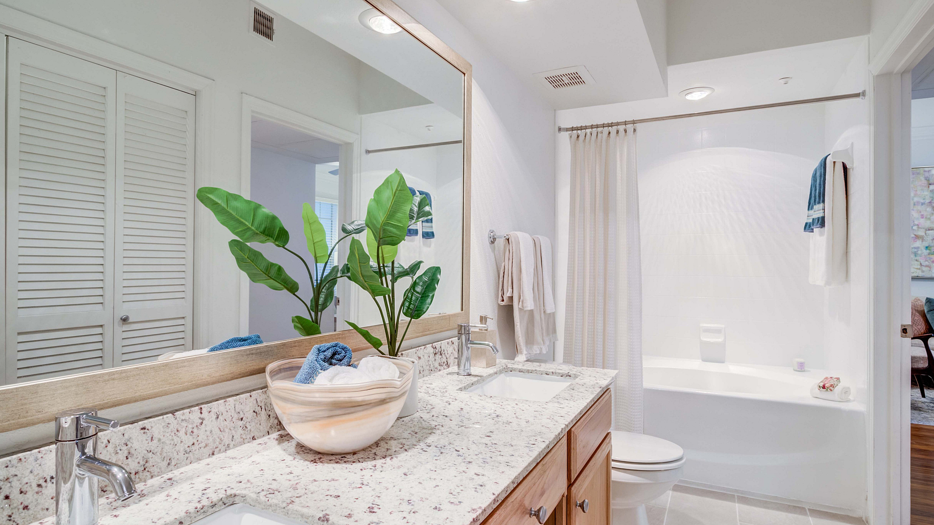 Bright bathroom featuring a sleek dual-sink vanity with granite countertops, vibrant green plant decor, and a spacious bathtub with elegant fixtures.