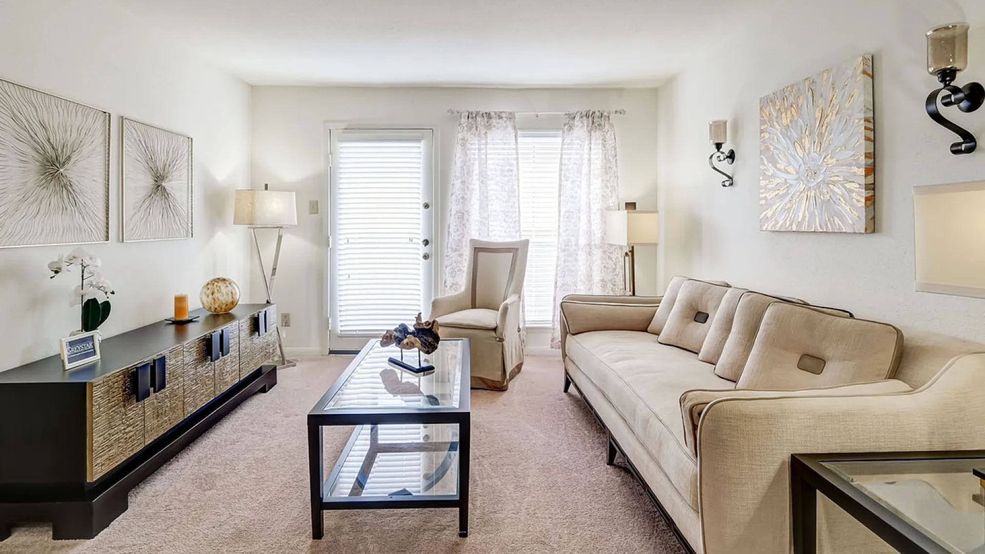 Bright, cozy living room with elegant decor, featuring a plush beige sofa, chic artwork, and abundant natural light through large windows.