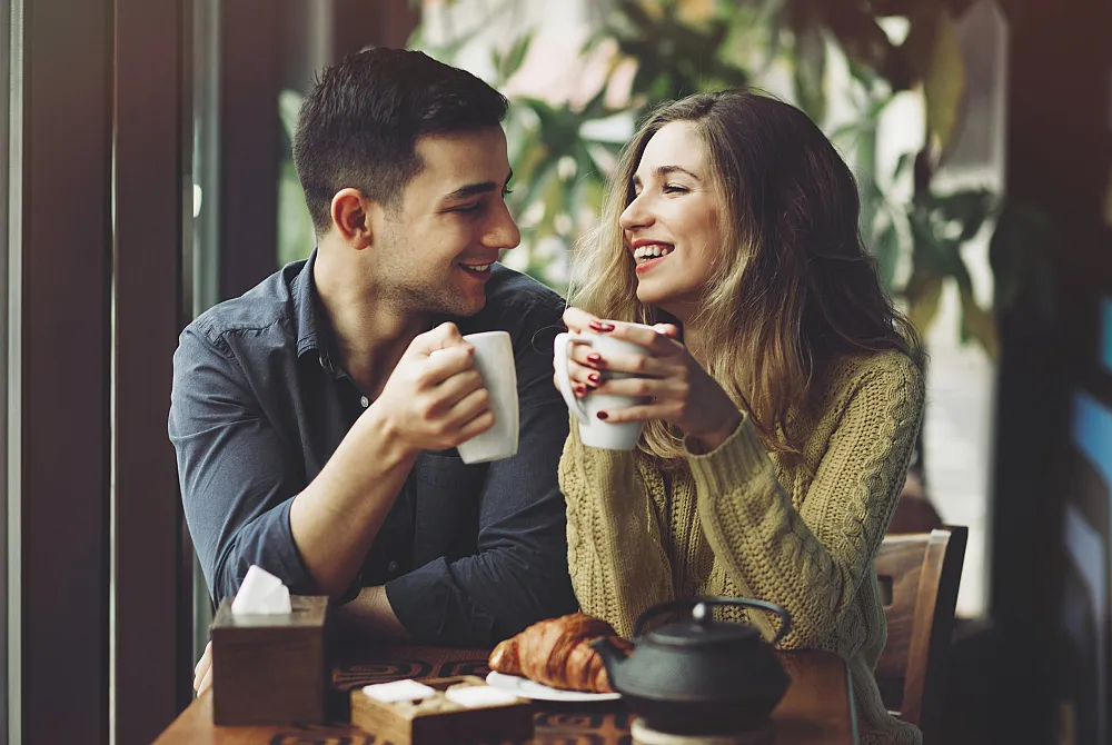 Cozy caf&eacute; scene with a joyful couple enjoying coffee and freshly baked croissants.