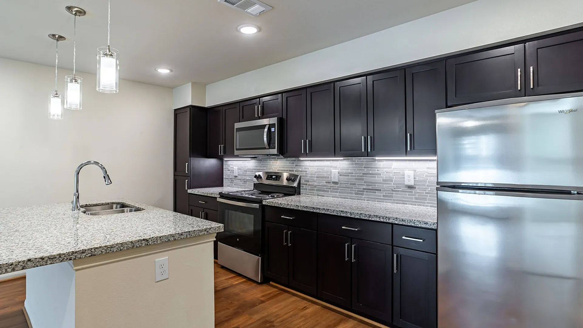 Modern kitchen with sleek dark cabinetry, stainless steel appliances, and elegant pendant lighting over a granite countertop island.