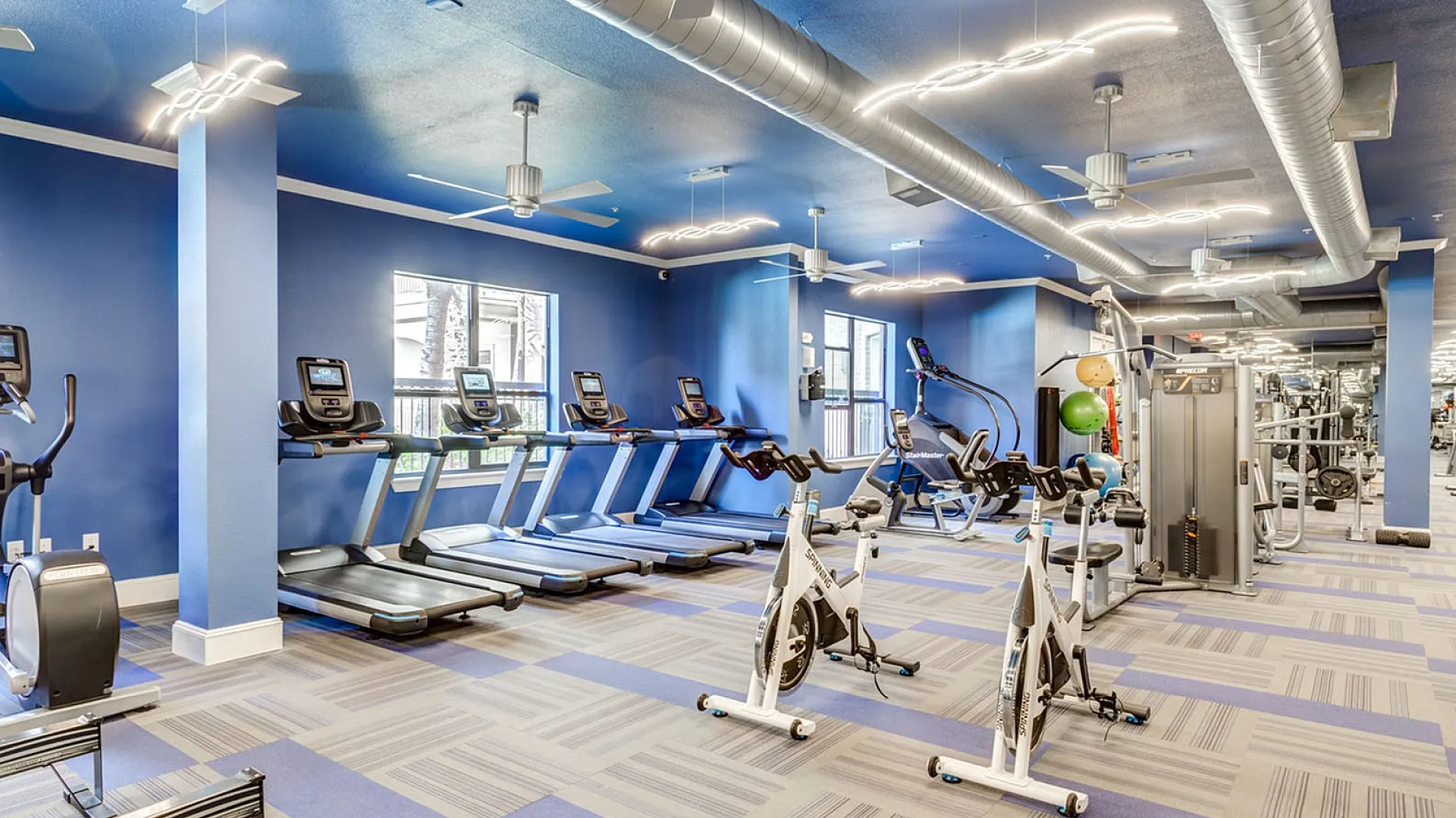 Modern fitness center with state-of-the-art treadmills, stationary bikes, and exercise equipment in a vibrant, well-lit space.