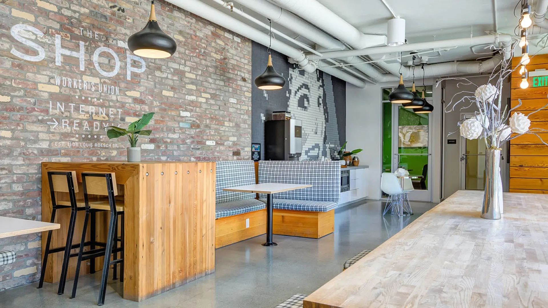 Trendy industrial-style communal area featuring exposed brick walls, modern pendant lighting, and cozy seating with a chic wooden table.