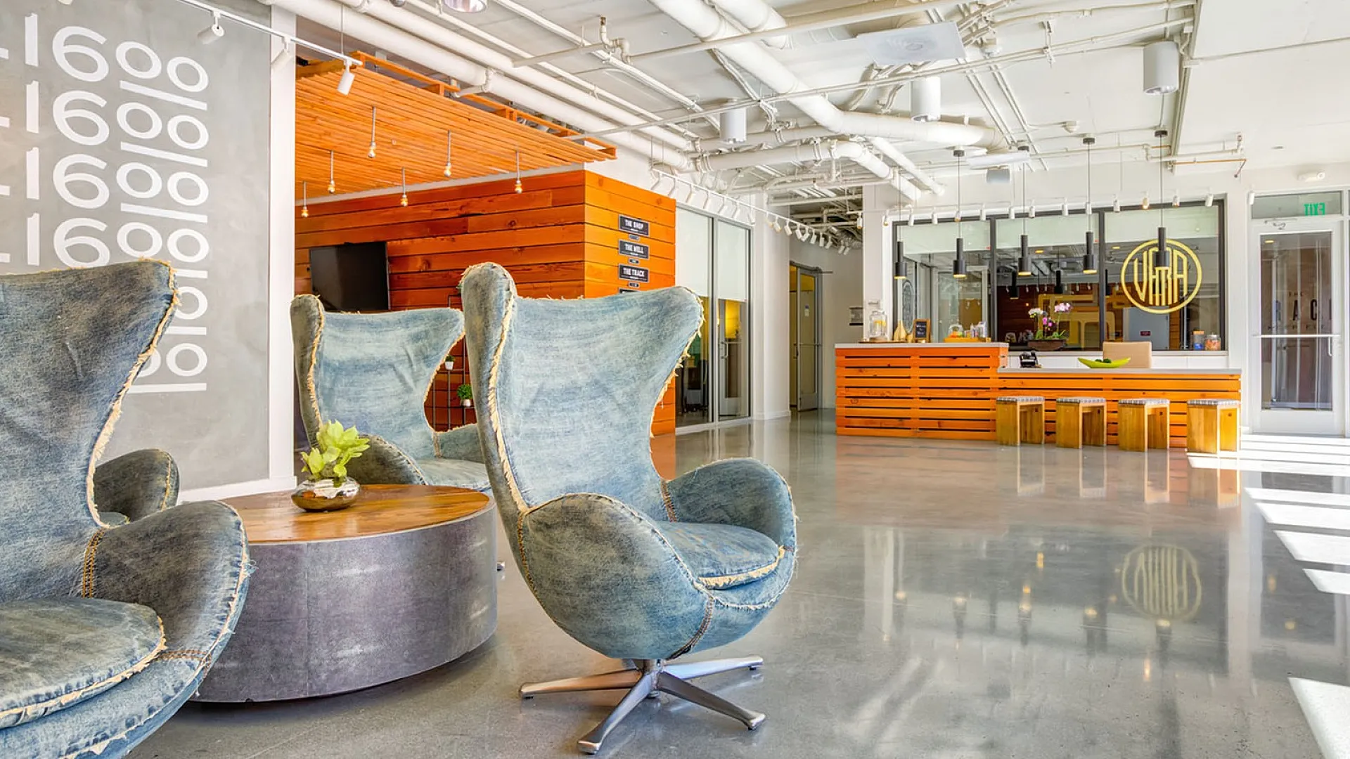 Modern lobby with stylish denim wingback chairs, sleek polished concrete floors, and a warm wooden reception area under contemporary lighting.